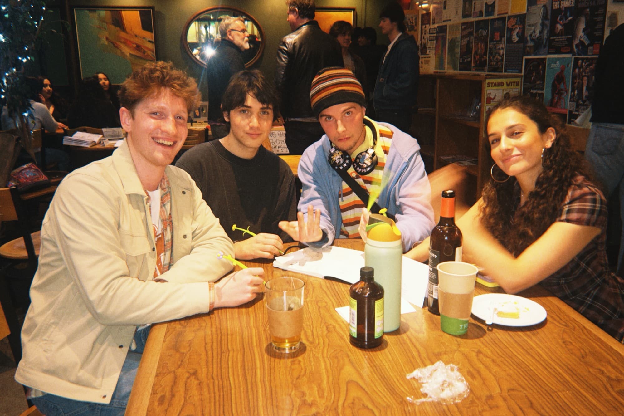 Three men and a woman smiling at the camera around a bar table with drinks and posters behind
