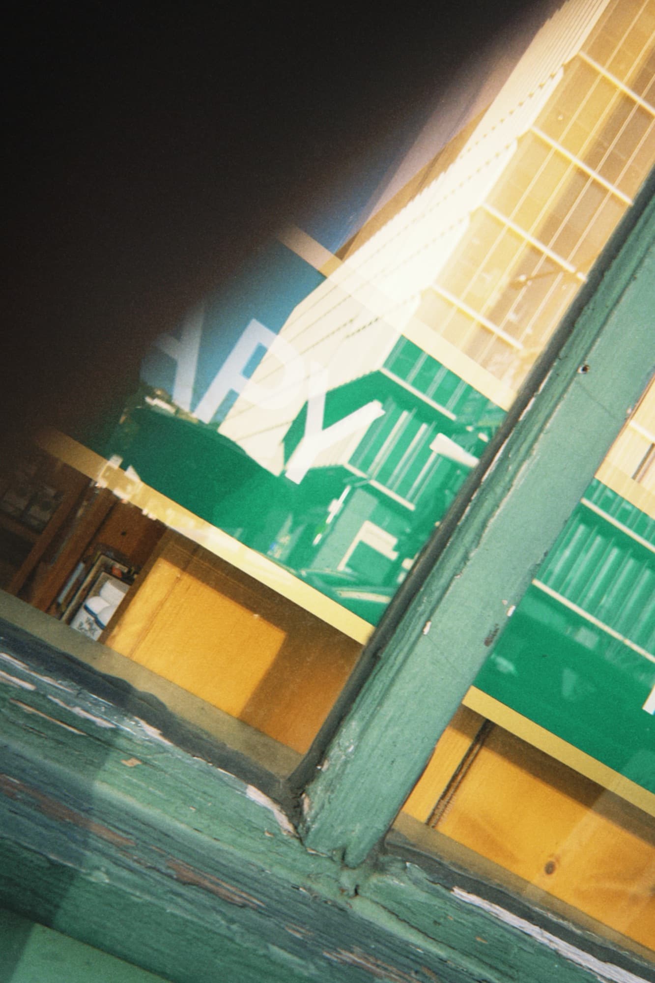 Double-exposed photo layering a green wood window frame over a partial storefront sign