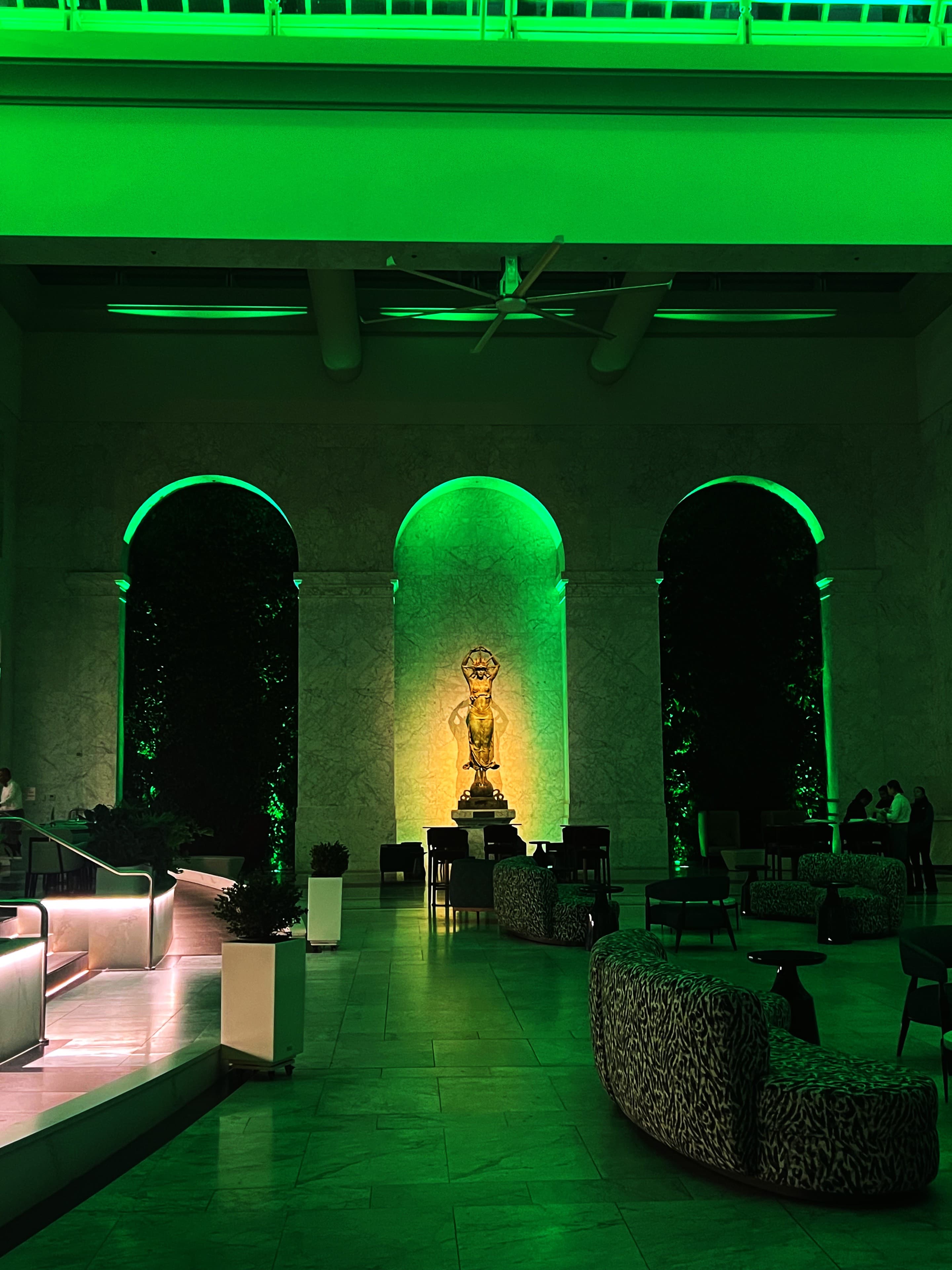 Marble hotel lobby lit in green with a small statue on a pedestal and animal-print armchairs