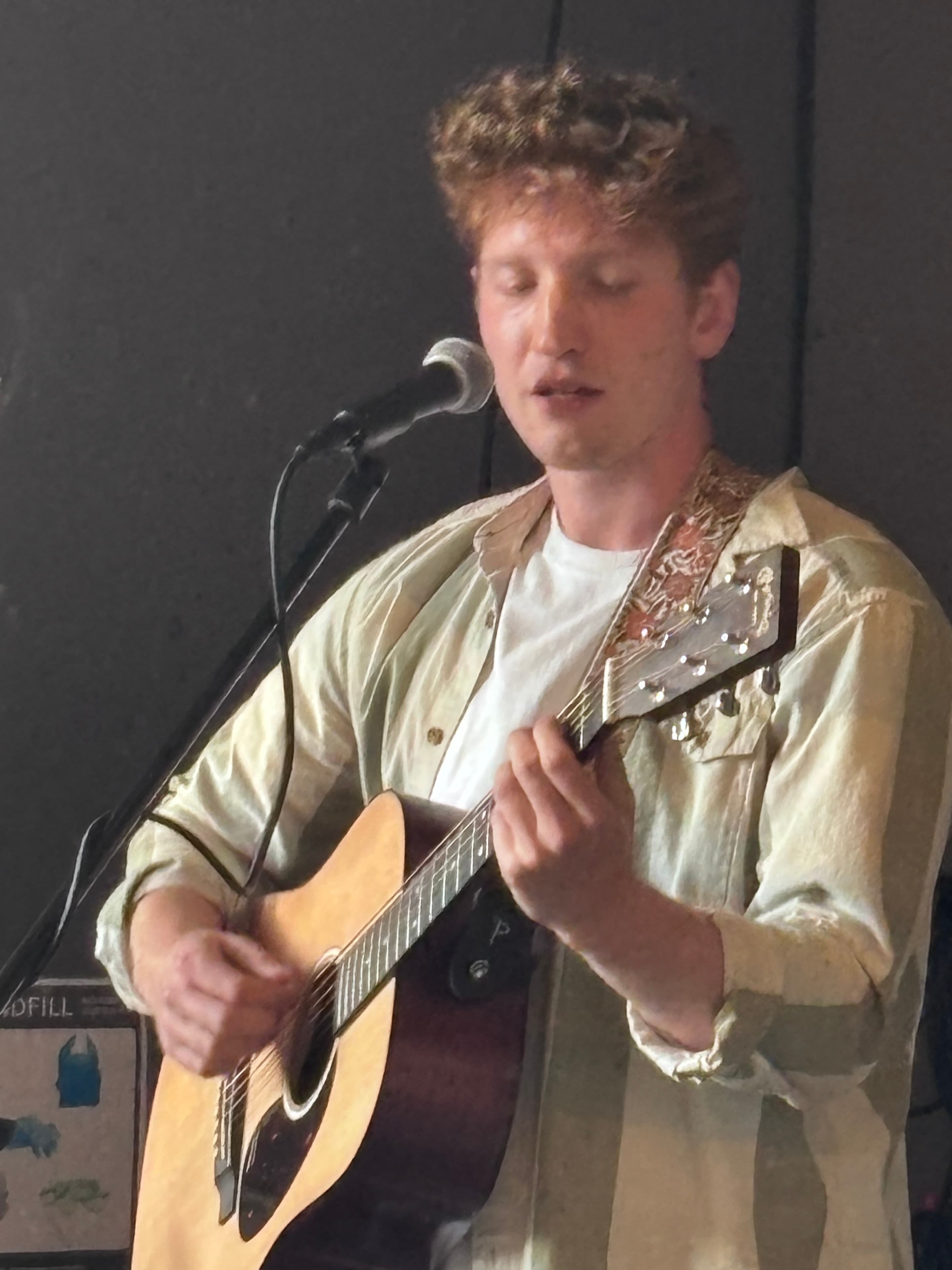 Close-up of a man singing with eyes closed while playing an acoustic guitar into a microphone