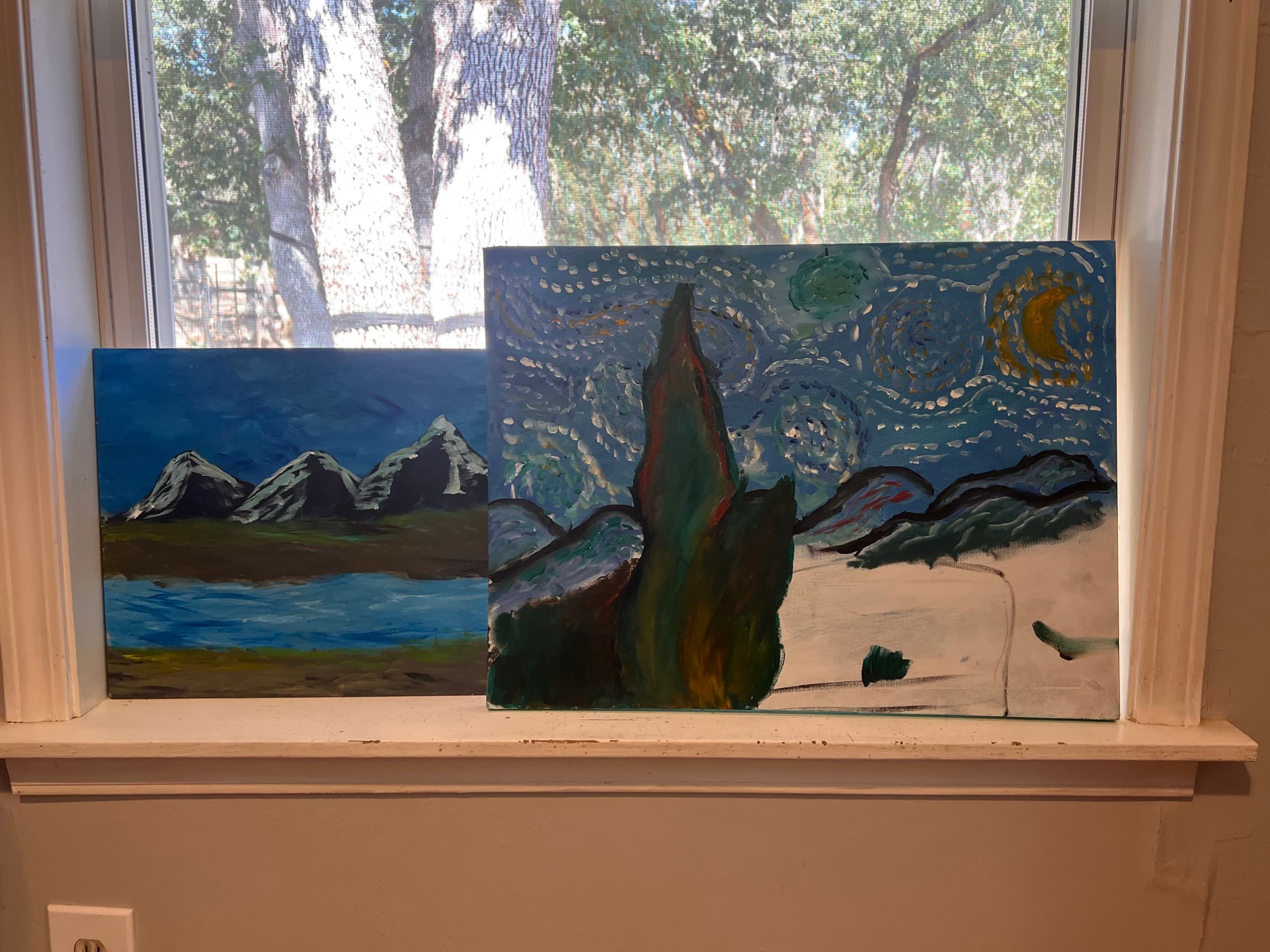 Two paintings on a windowsill, a blue mountain lake scene and a swirling starry sky with a tall dark tree